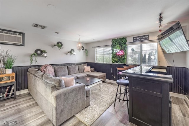 living area featuring visible vents, wood walls, an AC wall unit, a wainscoted wall, and light wood-style flooring