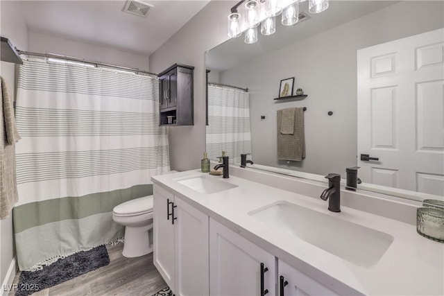bathroom featuring a sink, toilet, wood finished floors, and visible vents