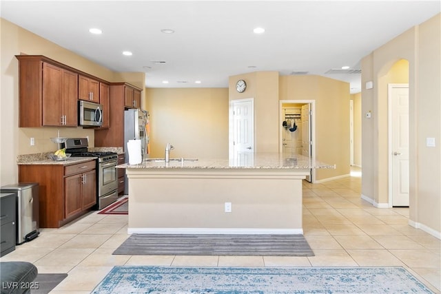 kitchen featuring a kitchen island with sink, stainless steel appliances, brown cabinets, and light tile patterned flooring