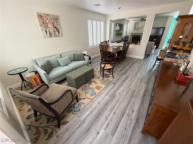 living area with a ceiling fan, visible vents, a tile fireplace, wood finished floors, and baseboards