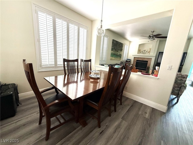 dining room with a ceiling fan, baseboards, wood finished floors, and a tile fireplace