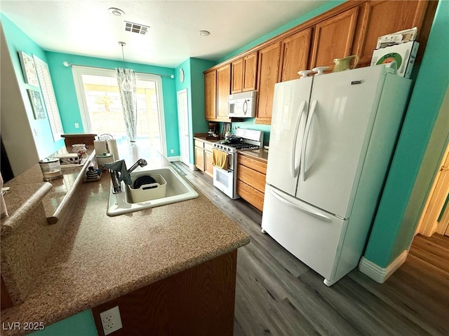 kitchen featuring visible vents, brown cabinetry, dark wood-style flooring, white appliances, and a sink