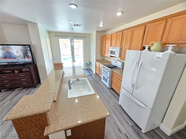 10071 Lemon Valley Ave, Las Vegas, NV 89147 - kitchen featuring white appliances, a sink, a center island with sink, wood finished floors, and light stone countertops