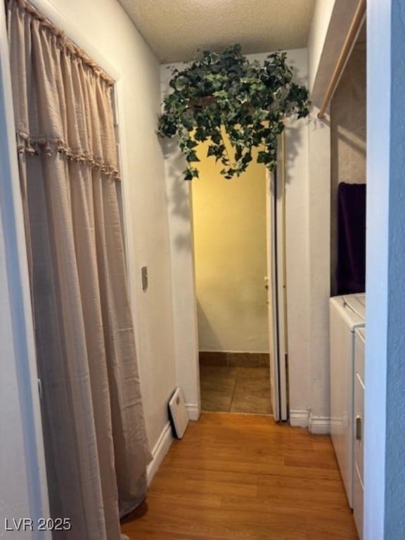 hall with light wood-style floors, a textured ceiling, and washer and dryer
