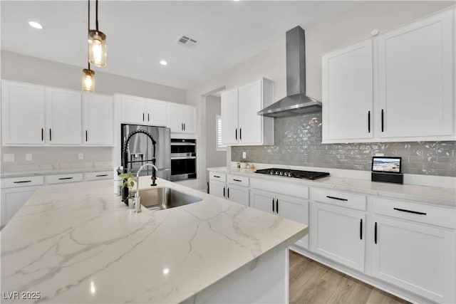 kitchen with wall chimney range hood, gas cooktop, stainless steel double oven, visible vents, and a sink