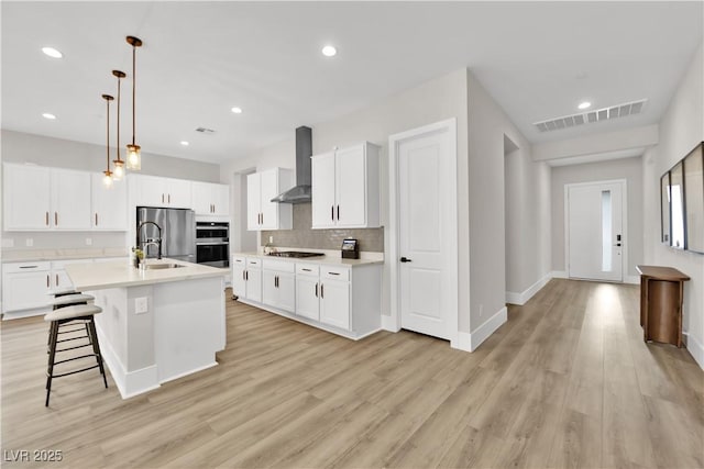 kitchen featuring wall chimney range hood, appliances with stainless steel finishes, light countertops, and visible vents