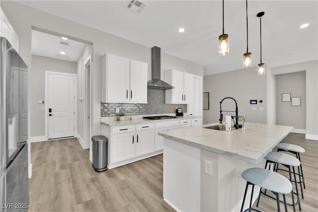 kitchen with a kitchen breakfast bar, visible vents, light wood-type flooring, a sink, and wall chimney exhaust hood