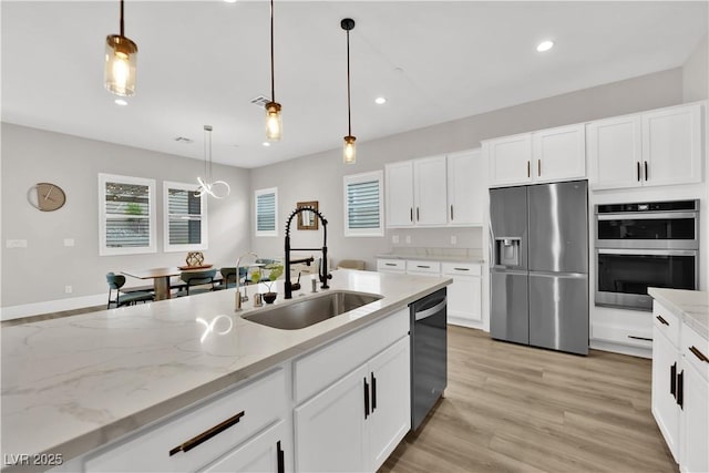 kitchen featuring light stone countertops, white cabinets, a sink, appliances with stainless steel finishes, and decorative light fixtures
