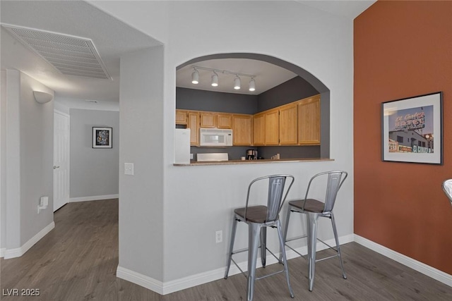 kitchen featuring visible vents, track lighting, wood finished floors, white appliances, and baseboards