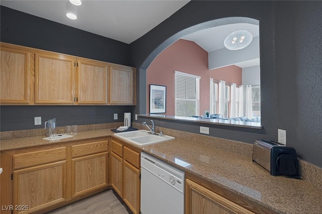 kitchen featuring white dishwasher, arched walkways, a sink, light brown cabinets, and light wood-style flooring