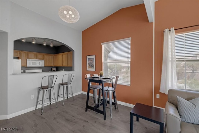 dining room with wood finished floors, arched walkways, baseboards, and lofted ceiling