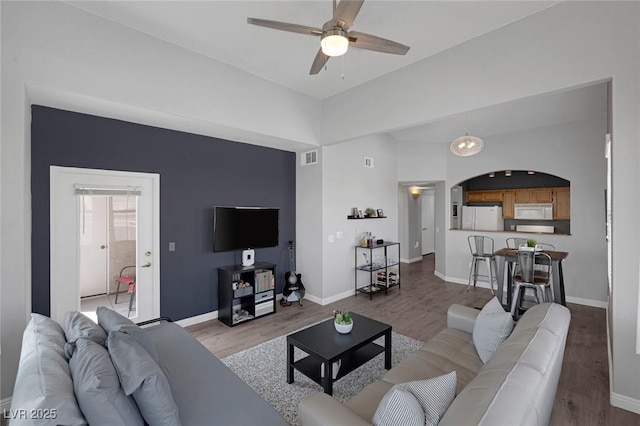 living area featuring a ceiling fan, visible vents, arched walkways, baseboards, and light wood finished floors