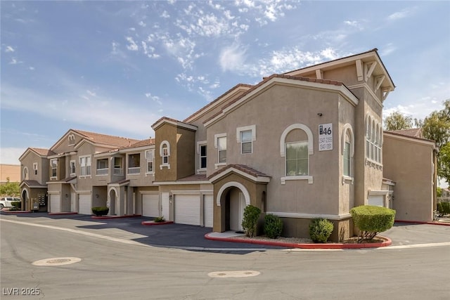 view of front of property with driveway, a tile roof, a residential view, an attached garage, and stucco siding