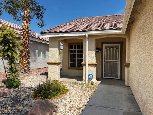 view of exterior entry with stucco siding and a tiled roof