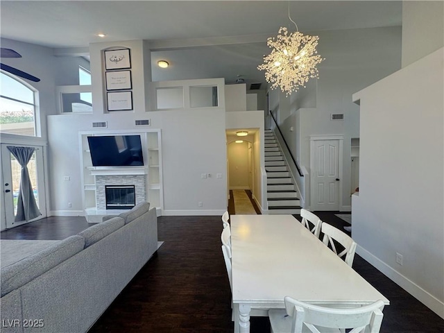 dining area with a high ceiling, stairs, a fireplace, a chandelier, and dark wood finished floors