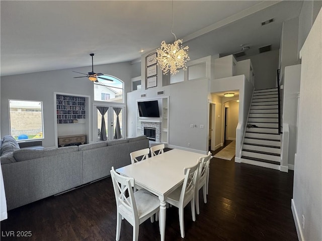 dining space with a fireplace, ceiling fan, dark wood finished floors, stairs, and high vaulted ceiling