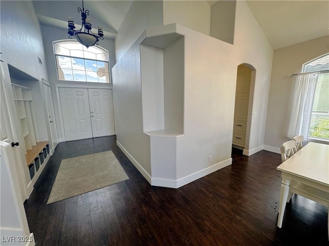 entryway with high vaulted ceiling, arched walkways, dark wood-type flooring, and a chandelier