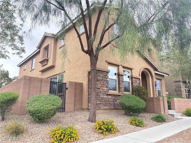view of side of property with a gate, stucco siding, stone siding, and fence