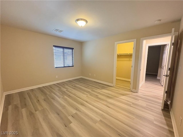 unfurnished bedroom featuring visible vents, a closet, baseboards, a spacious closet, and light wood finished floors