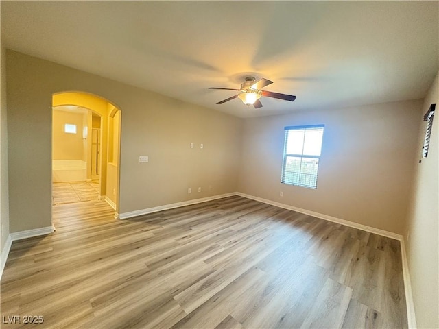 spare room with arched walkways, ceiling fan, baseboards, and light wood-style flooring