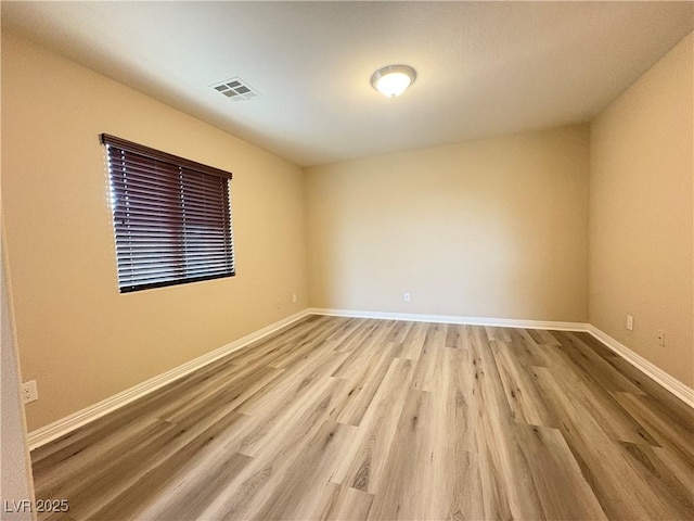 empty room with baseboards, light wood finished floors, and visible vents