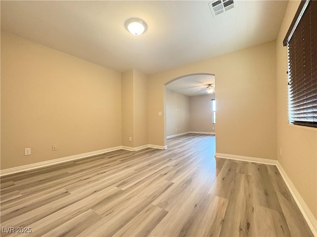 empty room with visible vents, baseboards, ceiling fan, arched walkways, and light wood finished floors