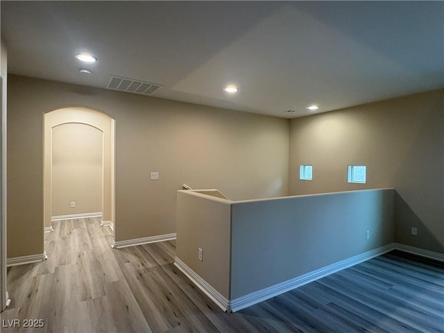 hallway featuring arched walkways, recessed lighting, baseboards, wood finished floors, and visible vents