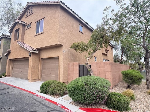 exterior space with fence, stucco siding, a tiled roof, concrete driveway, and an attached garage
