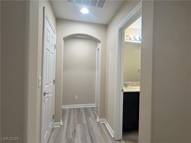 corridor with visible vents, arched walkways, baseboards, light wood-style floors, and recessed lighting