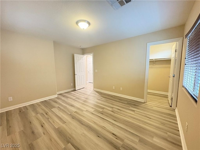 unfurnished bedroom with baseboards, visible vents, light wood-style flooring, and a spacious closet