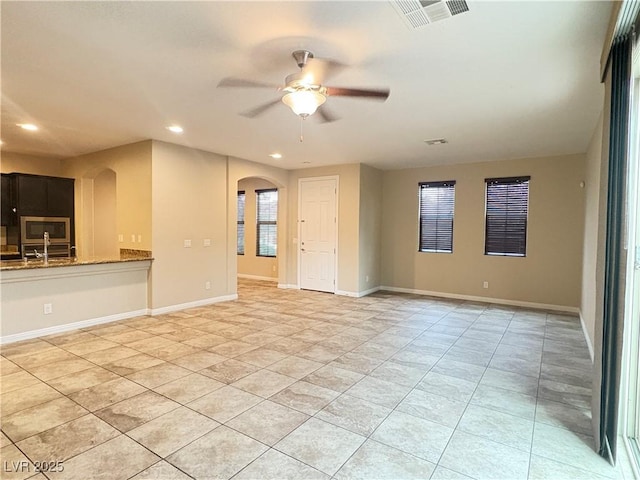 unfurnished living room featuring arched walkways, a ceiling fan, baseboards, recessed lighting, and visible vents
