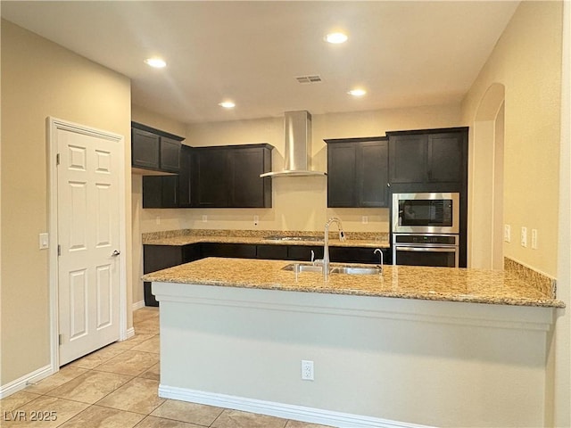 kitchen featuring a sink, appliances with stainless steel finishes, light stone counters, and wall chimney exhaust hood
