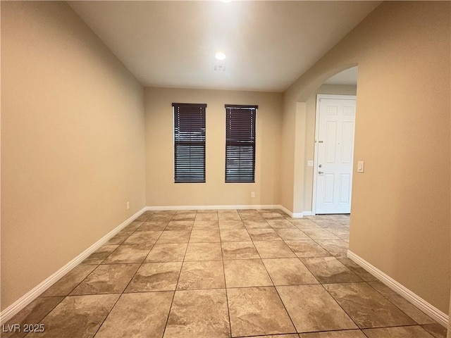 spare room with light tile patterned floors, arched walkways, and baseboards