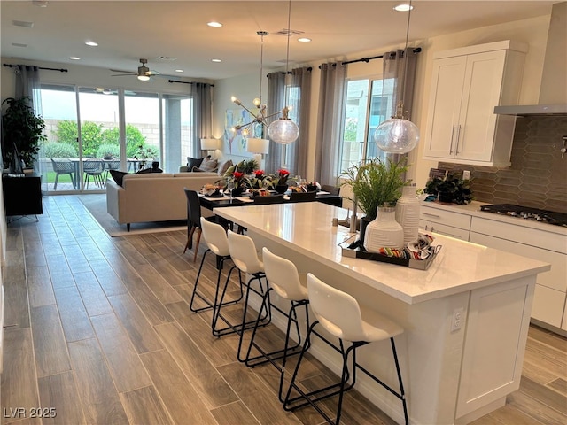 929 Hunter Shores Ave, North Las Vegas, NV 89084 - kitchen with wall chimney exhaust hood, black gas cooktop, a center island, white cabinetry, and ceiling fan