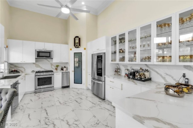 kitchen with a towering ceiling, white cabinets, light stone counters, a sink, and stainless steel appliances