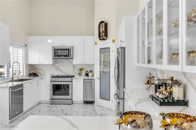 kitchen featuring white cabinets, a sink, marble finish floor, stainless steel appliances, and glass insert cabinets