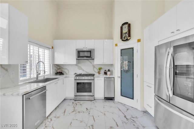 kitchen featuring a high ceiling, appliances with stainless steel finishes, a sink, marble finish floor, and white cabinetry