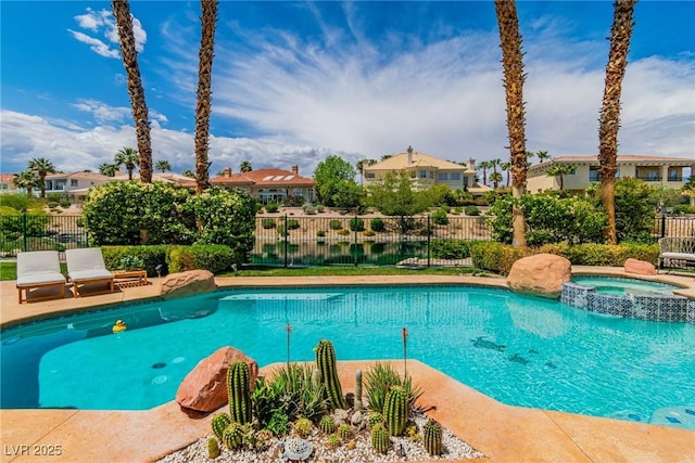 view of swimming pool featuring a pool with connected hot tub, fence, and a residential view