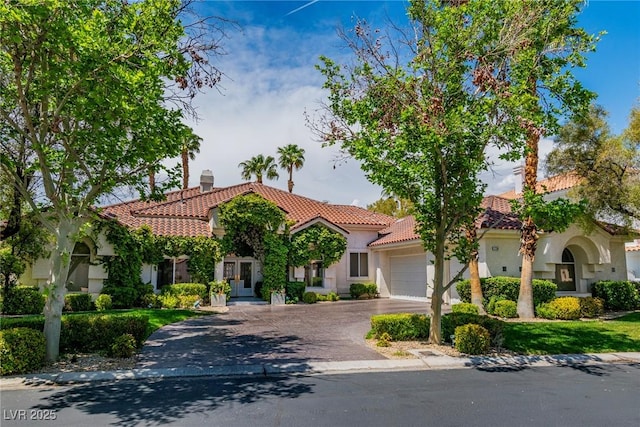 mediterranean / spanish house featuring a garage, a tiled roof, driveway, and stucco siding