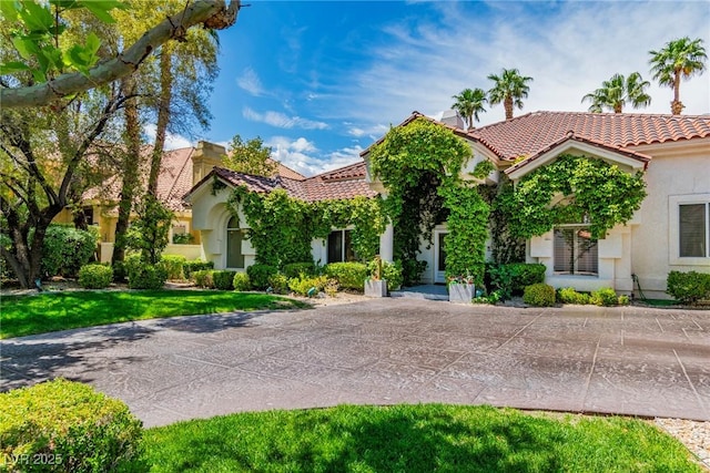 mediterranean / spanish home featuring a tiled roof, a chimney, and stucco siding