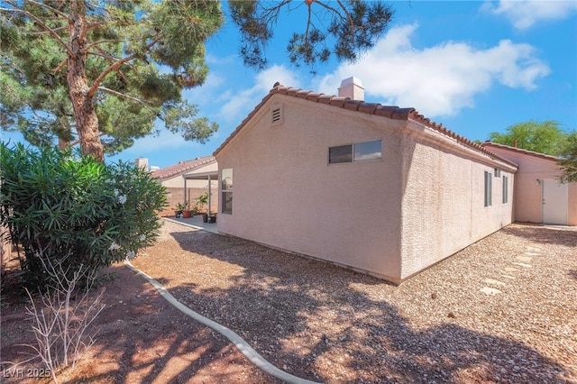 view of side of property with a chimney, stucco siding, and a tiled roof