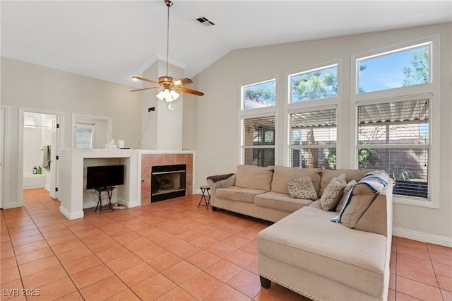 living area with light tile patterned floors, baseboards, a tiled fireplace, vaulted ceiling, and a ceiling fan