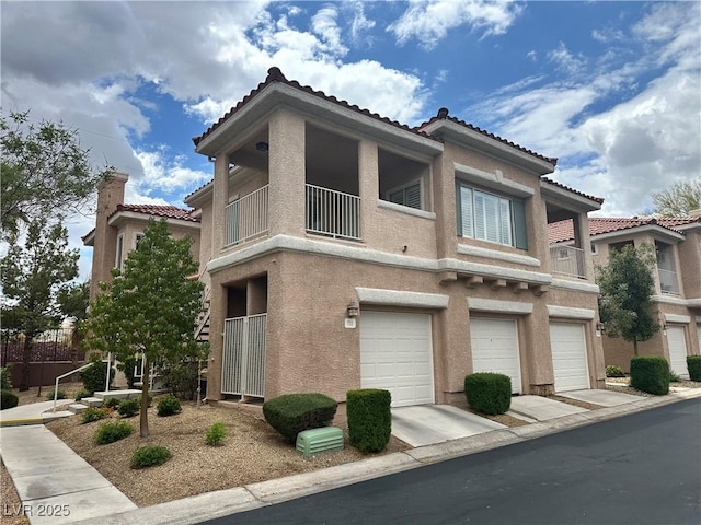 view of property featuring stucco siding, an attached garage, a tiled roof, and a balcony