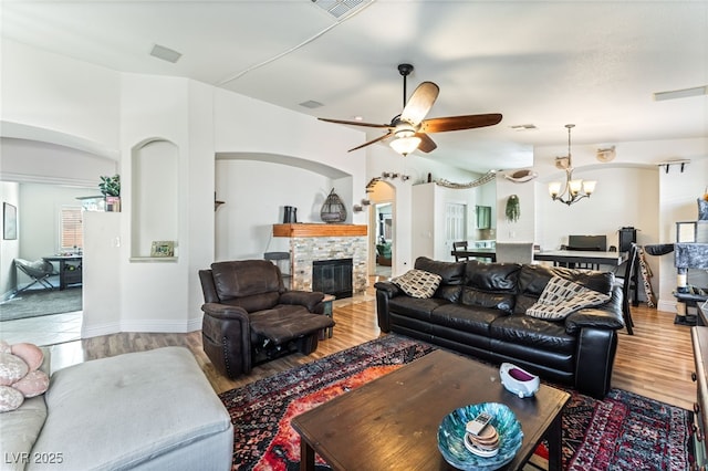living room with visible vents, arched walkways, a fireplace, wood finished floors, and ceiling fan with notable chandelier