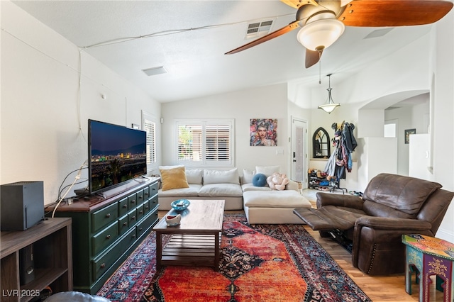 living room featuring a ceiling fan, visible vents, arched walkways, vaulted ceiling, and light wood-style flooring