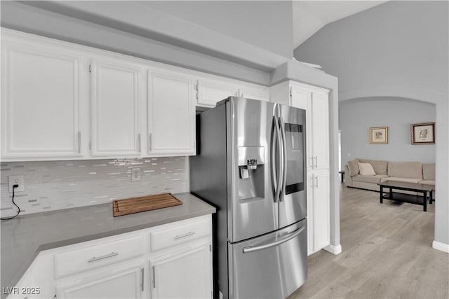 kitchen featuring white cabinets, stainless steel fridge, light wood-style floors, lofted ceiling, and backsplash