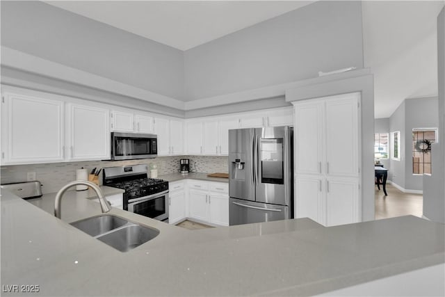 kitchen featuring decorative backsplash, light wood-type flooring, white cabinetry, a sink, and stainless steel appliances