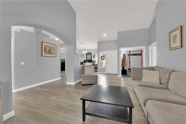 living area with arched walkways, baseboards, recessed lighting, and light wood-style floors