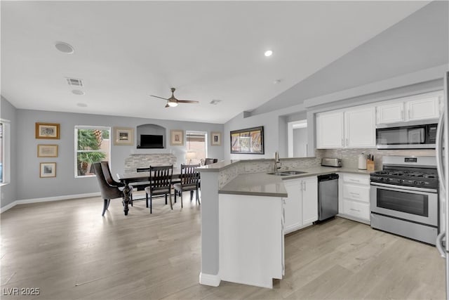 kitchen featuring appliances with stainless steel finishes, a sink, a peninsula, white cabinetry, and visible vents