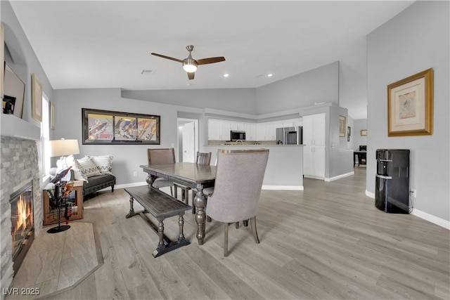 dining room with baseboards, light wood-style floors, ceiling fan, and vaulted ceiling